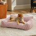 Small dog resting on a plush, textured pastel pink pet sofa bed in a cozy modern living room setting