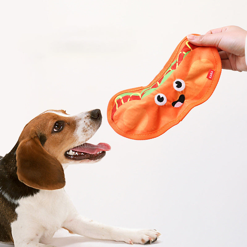 Beagle eagerly looking at a bright orange interactive chew toy shaped like a smiling hot dog.