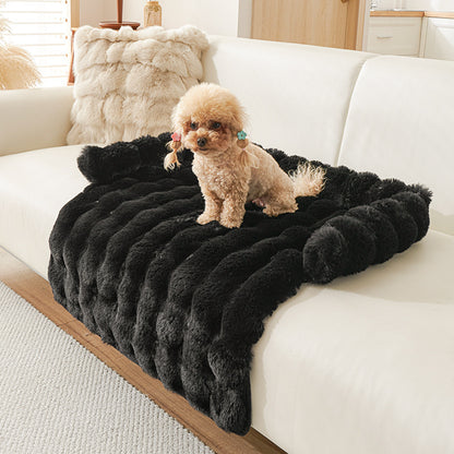 Small dog sitting on a thick, plush black pet mat draped over a modern white sofa in a bright living room