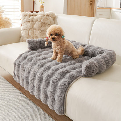 Small dog sitting on a plush, textured gray thermal mat draped over a white sofa in a modern living room
